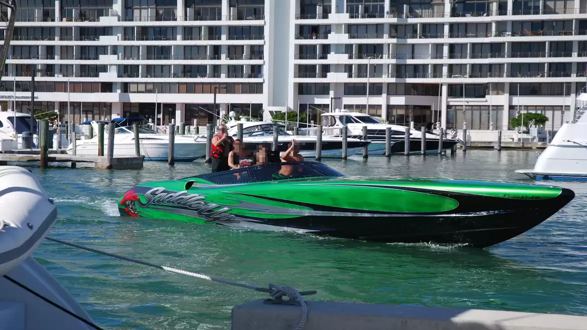 Green speedboat on water with modern buildings in the background.