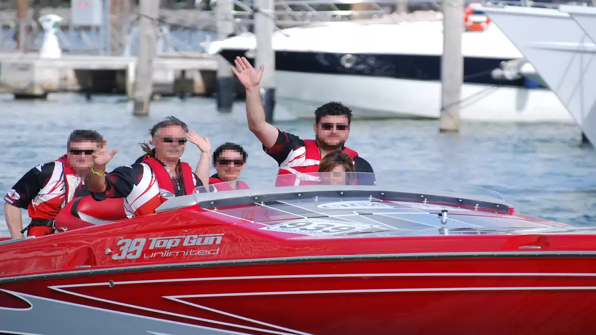 Group of people in a red speedboat driving in a marina.