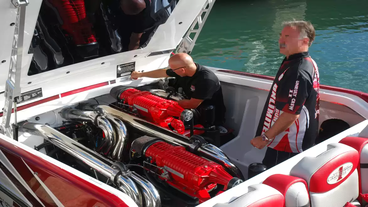 Two men inspecting the engine compartment of a high-speed boat with two powerful red engines.