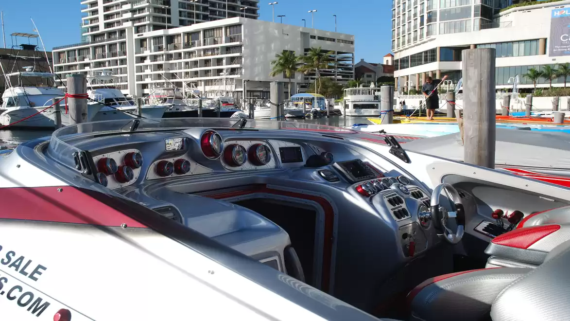 Modern speedboat cockpit with high-tech controls, docked in a marina with an urban backdrop.