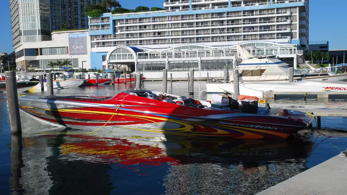 A sleek, red speedboat docked in the harbor with a modern hotel backdrop.