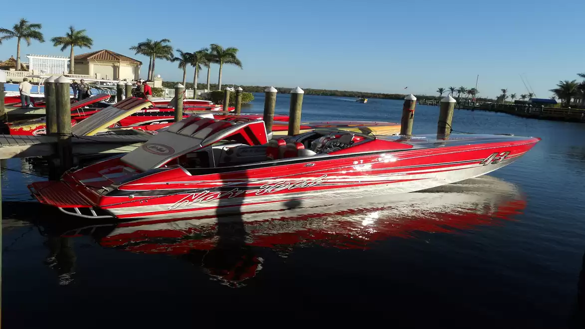 Red speedboat in the harbor under sunny skies, surrounded by palm trees and docks.