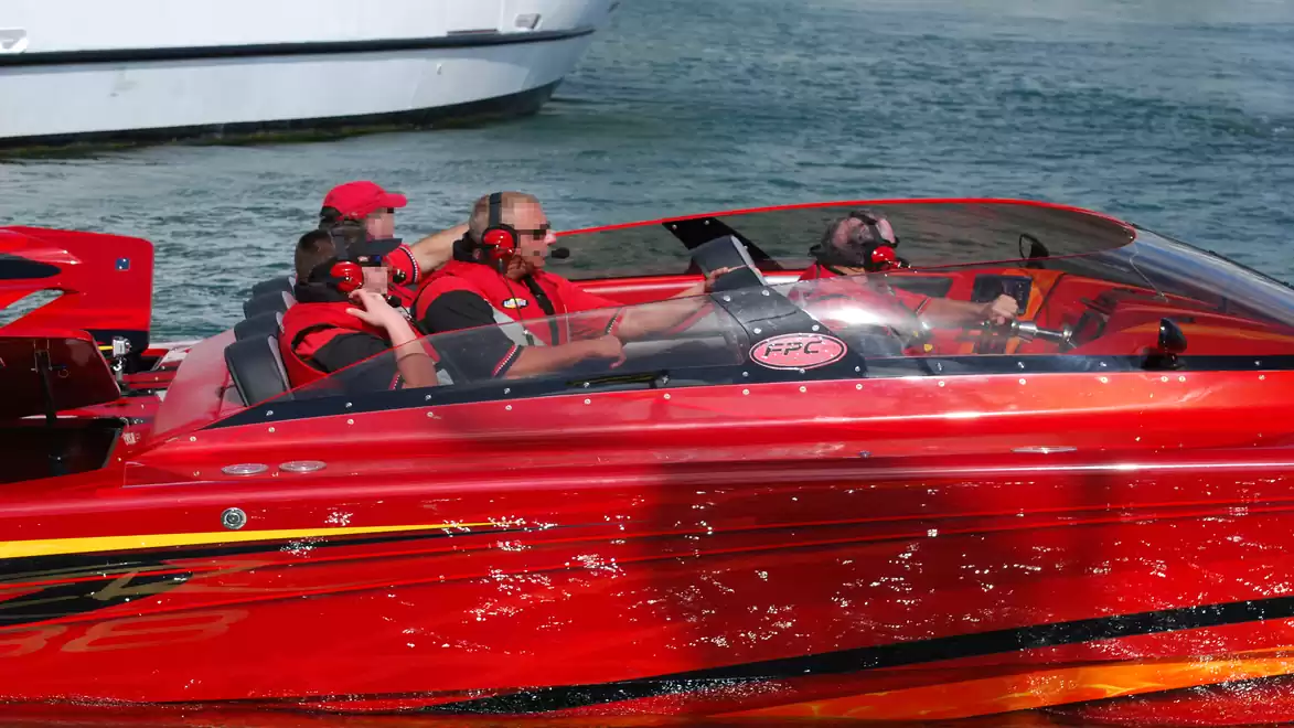 A red speedboat with several people in life jackets on the water.
