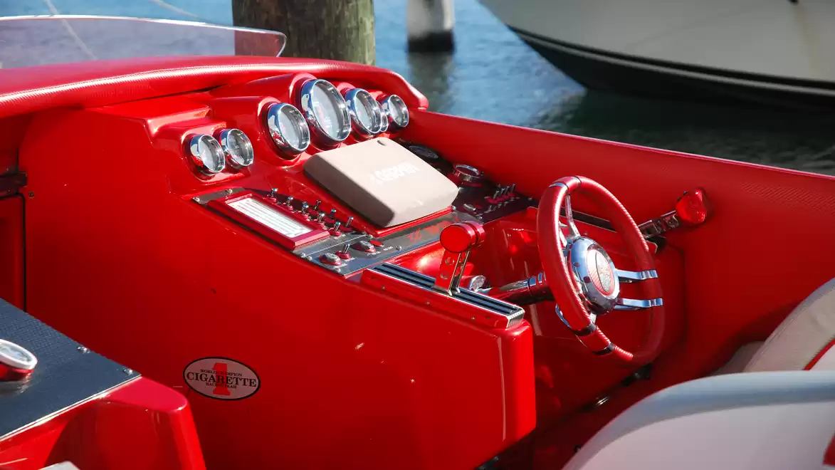 Close-up of a sleek, red boat cockpit with a shiny steering wheel and instruments at the water harbor.