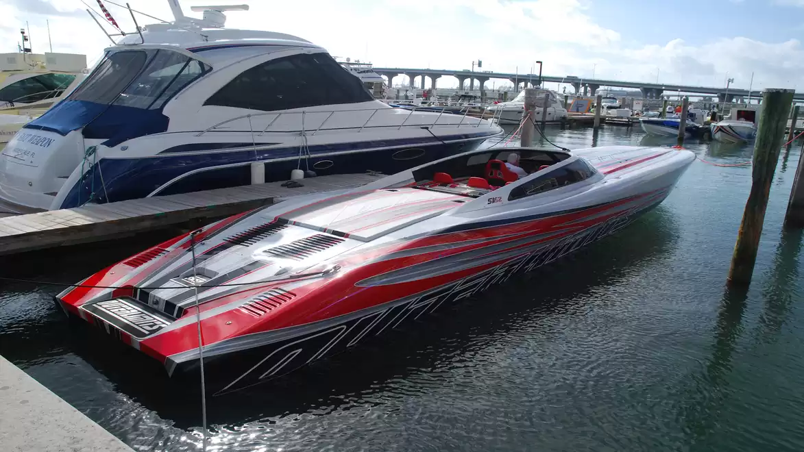 A sleek speedboat with red and silver paint is docked next to a yacht in the harbor.
