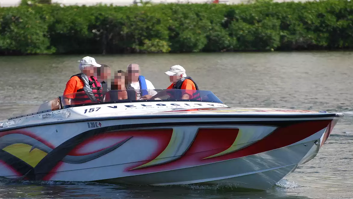 Speedboat on a river with four people on board wearing orange life jackets.