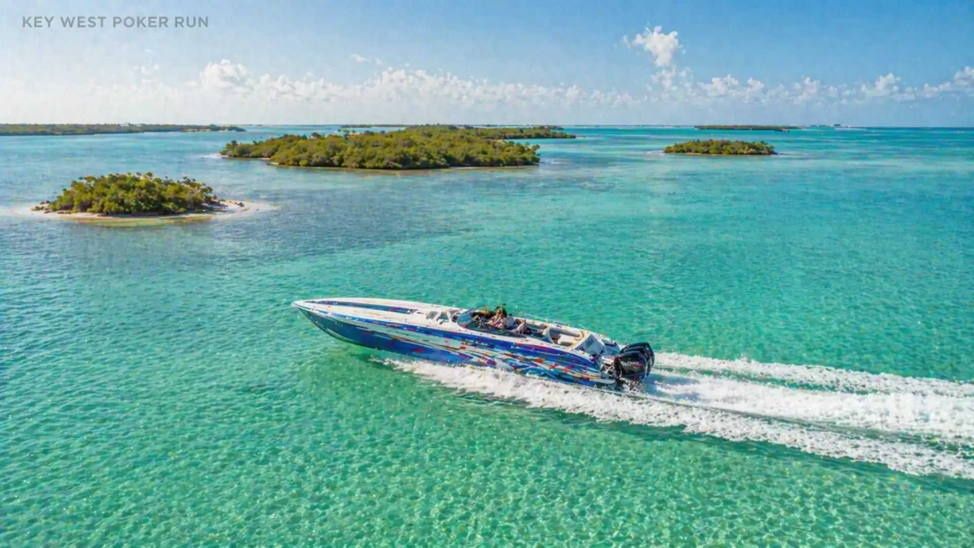 A speedboat travels through crystal clear water in a tropical setting with several small islands in the background under a blue sky.