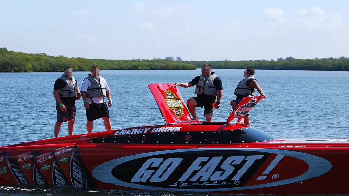 Four men stand on a red speedboat labeled 'GO FAST' on a calm lake.