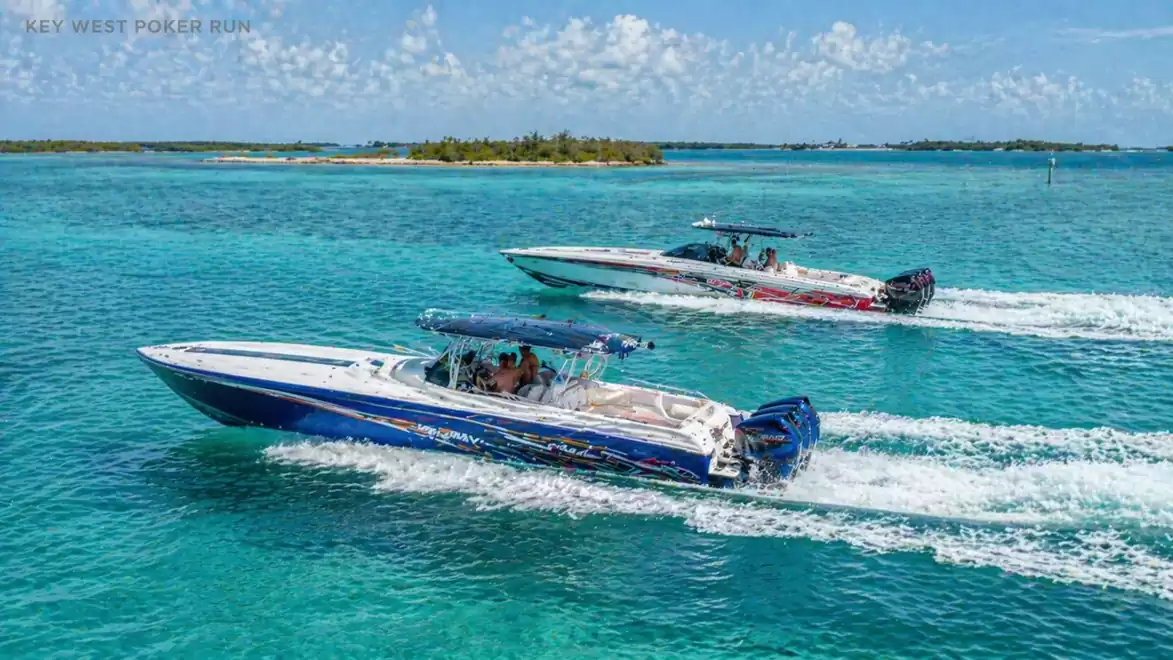 Two speedboats racing across the clear turquoise water under a sunny sky. A small, wooded island appears in the background.