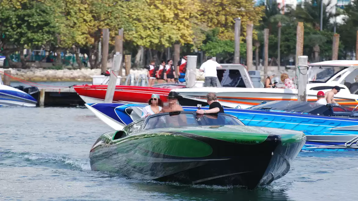 Several speedboats in a marina with trees in the background and people on the boats.