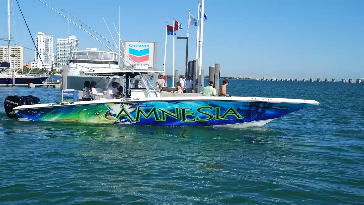 Sport boat with striking paint design moored in a bustling harbor under a clear blue sky.