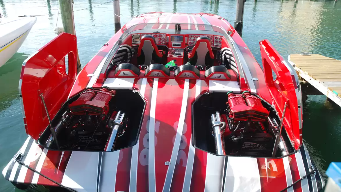 Sporty motorboat with open engine covers and red stripes, docked at a pier in the water.