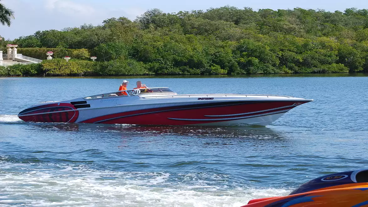 A stylish motorboat with a red and white design cruising on a calm lake against a wooded backdrop.