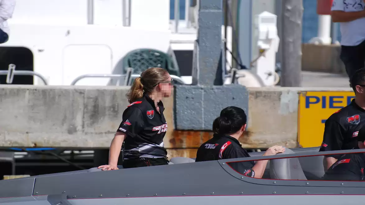 Three people in black polo shirts sitting on a boat in a harbor setting.