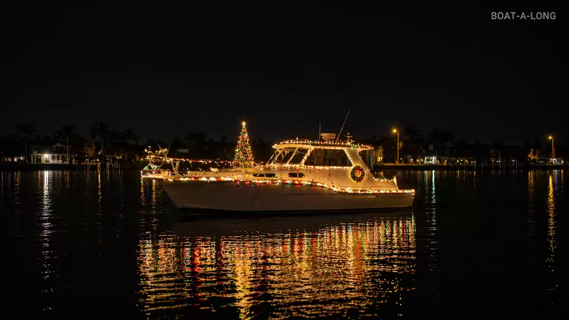 A lit boat with Christmas decorations moves on the water at night, with lights reflecting in the water.