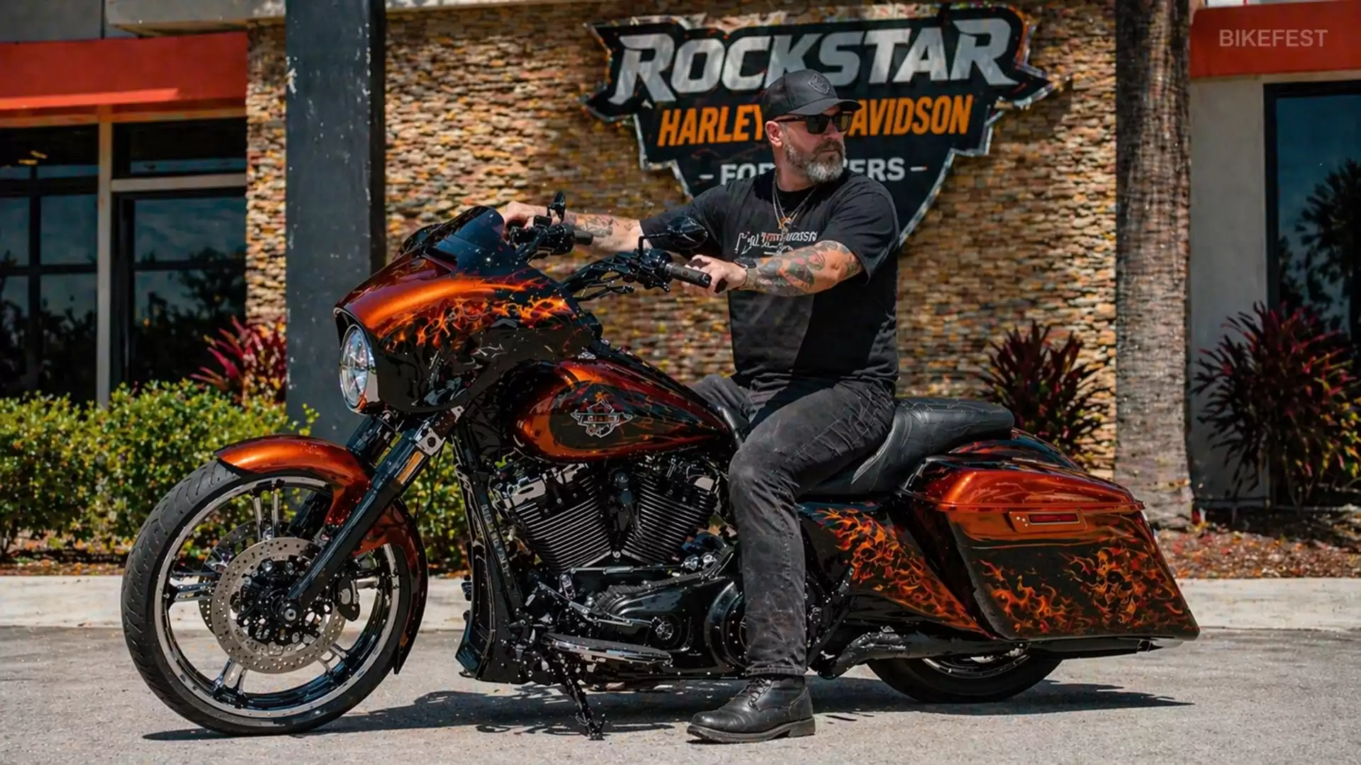 A man sits on a custom-designed motorcycle in front of the Rockstar Harley Davidson building.