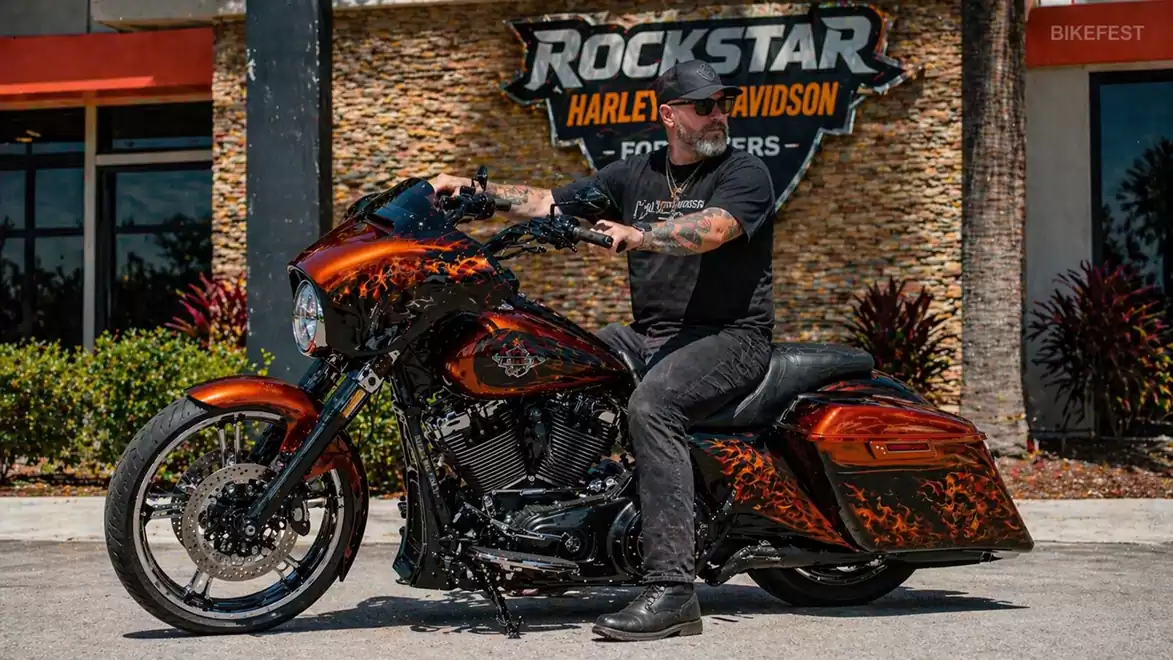 A man sits on a custom-designed motorcycle in front of the Rockstar Harley Davidson building.