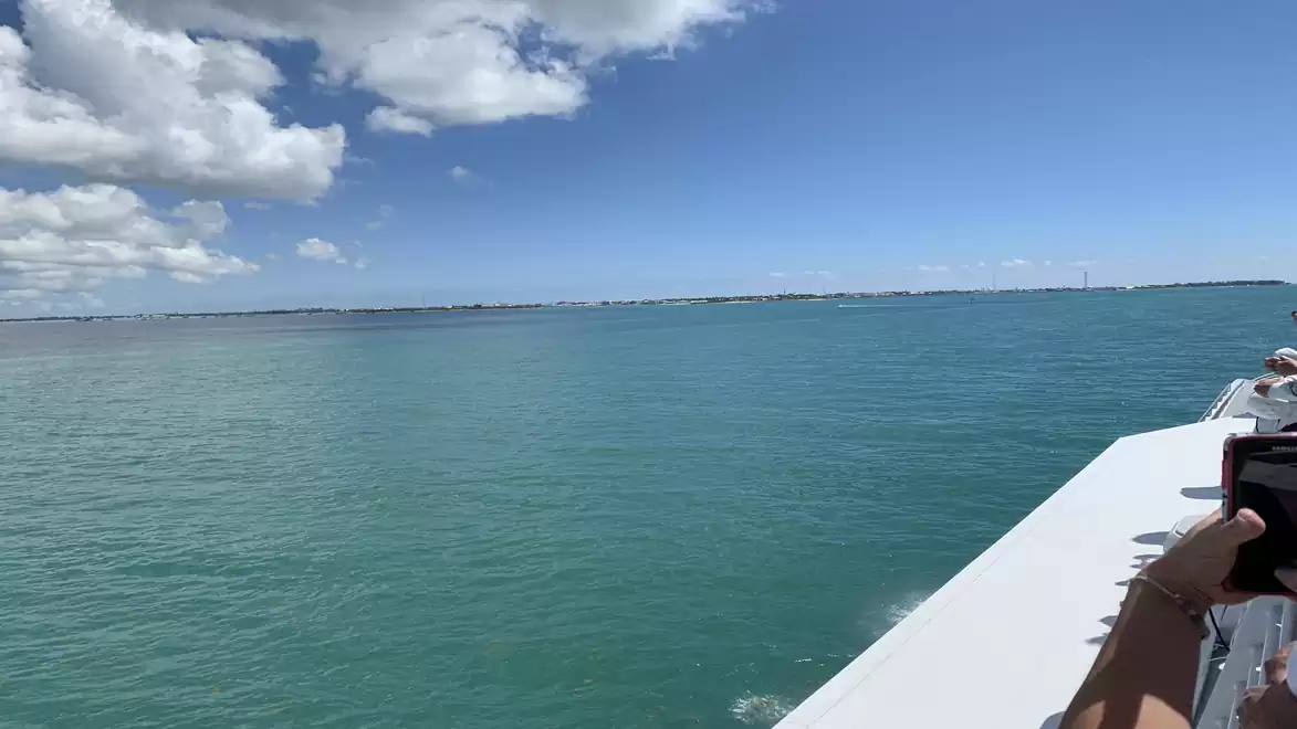 A large body of water with a clear blue sky and white clouds. On the right side of the image, there is a boat with a person taking a photo.