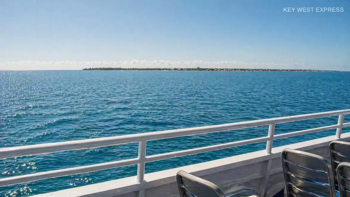 A boat ride on blue sea with a distant island on the horizon, clear skies, and sunlight reflecting on the water.