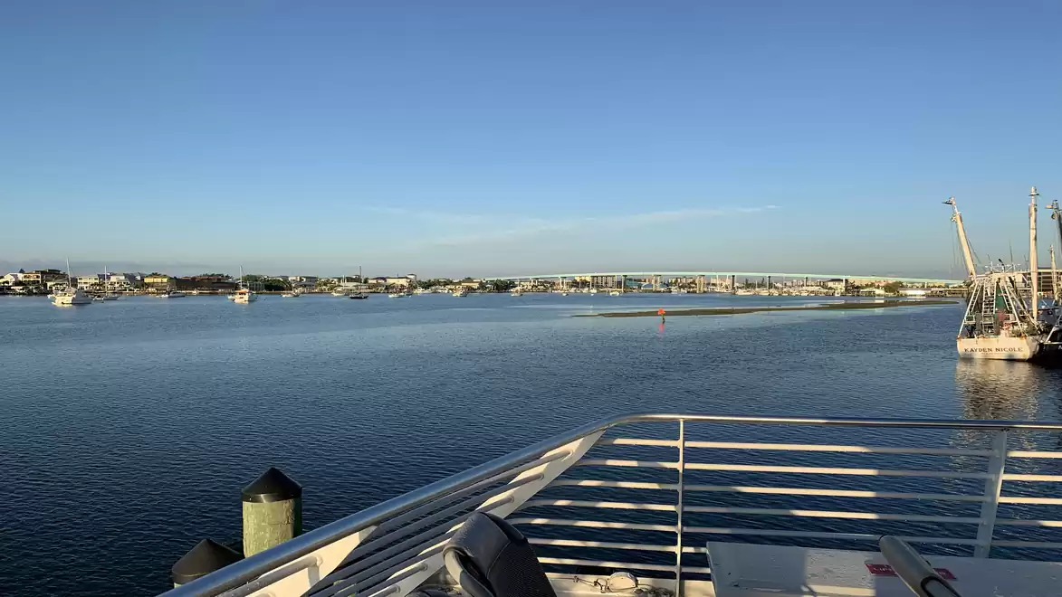 Harbor view with calm water, blue sky, and various boats along the shore.