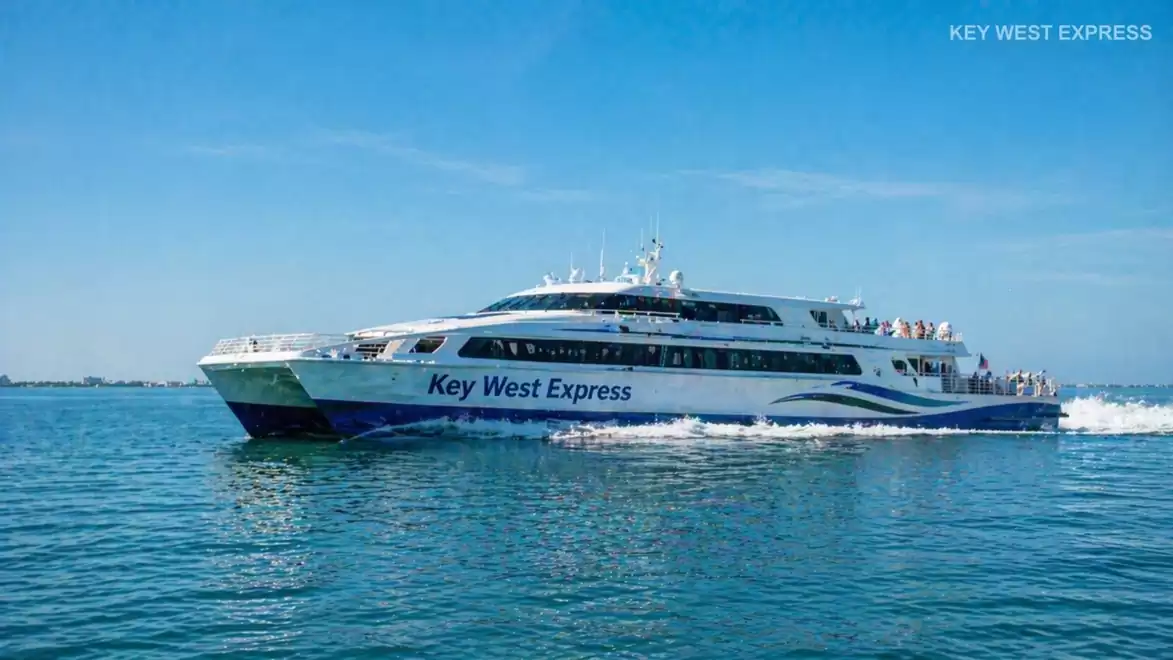 A modern Key West Express passenger ship sails on clear blue sea on a sunny day.
