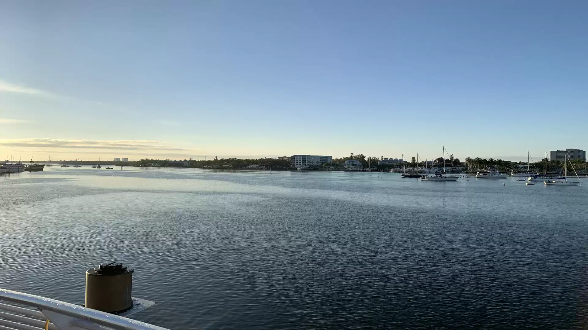 Panoramic view of a calm harbor at sunset with several sailboats and a vast, clear sky.