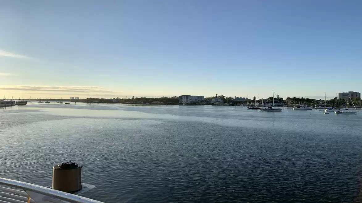 Panoramic view of a calm harbor at sunset with several sailboats and a vast, clear sky.