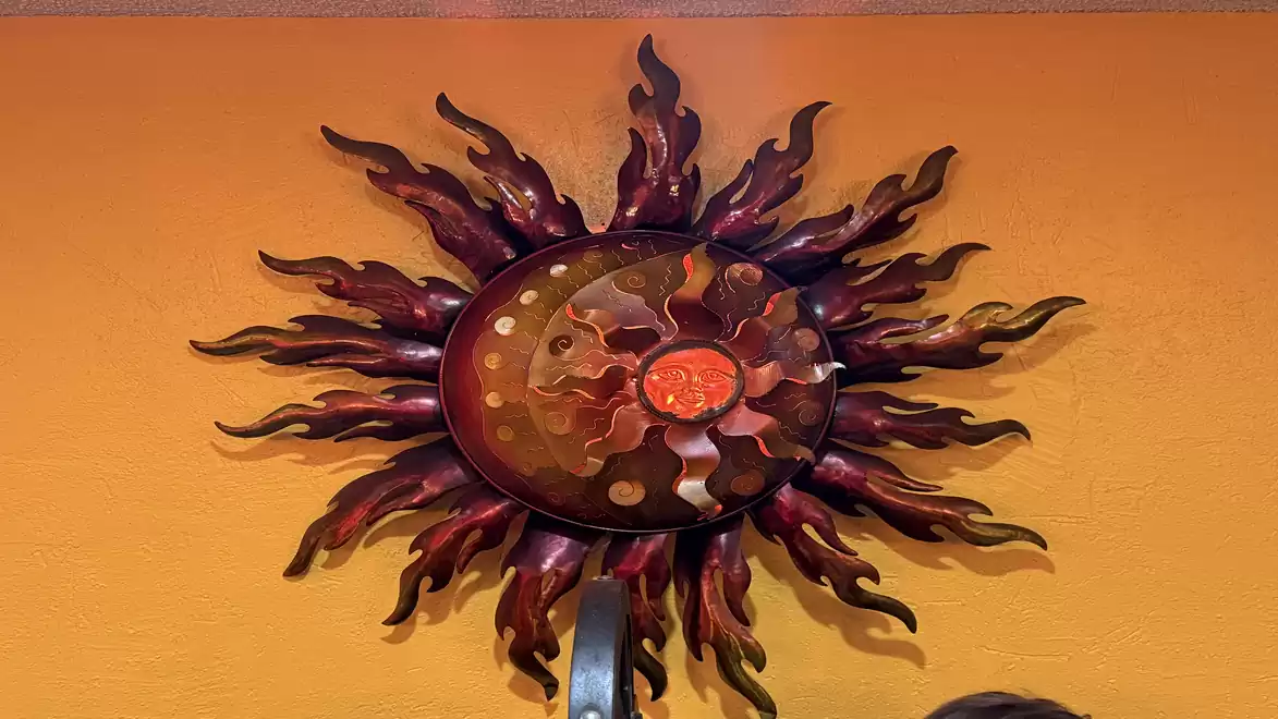 An artistic wall decoration in the shape of a sun with orange-red flames on an orange background.