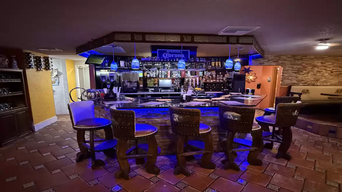 Cozy indoor bar with blue lighting and decorative, rustic chairs.
