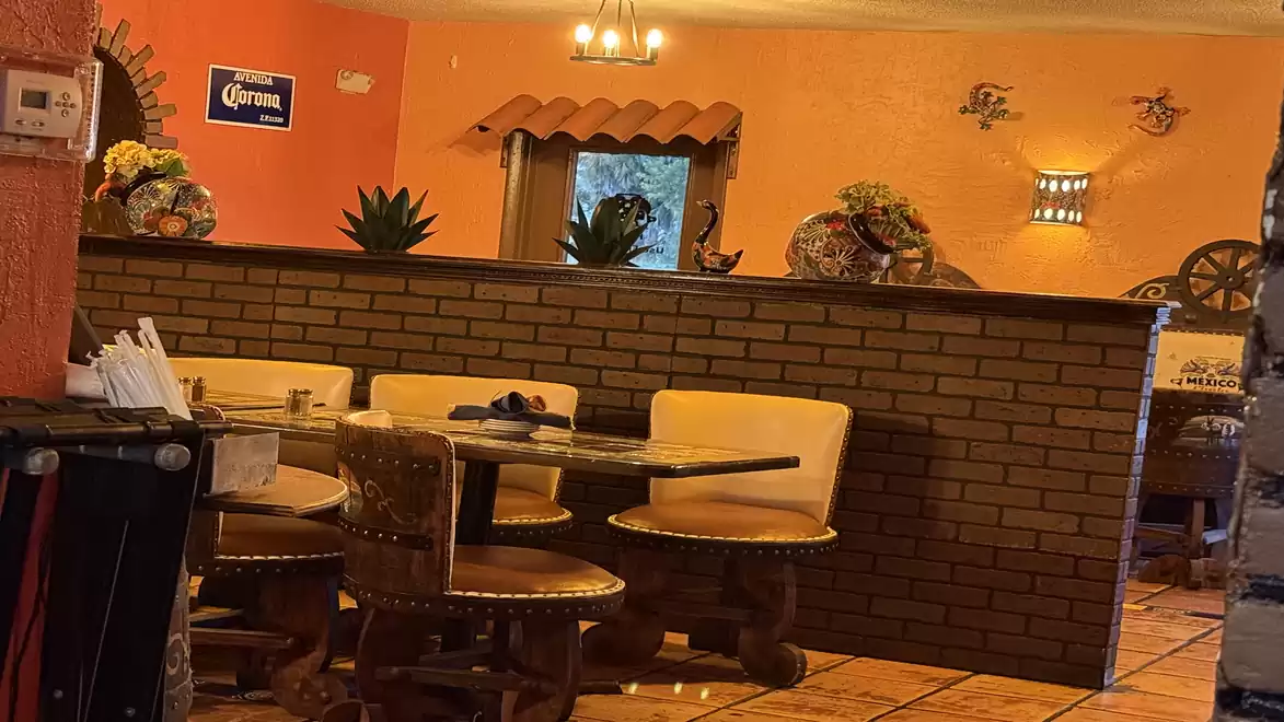 Cozy Mexican restaurant with wooden tables and chairs, brick wall, and decorative elements on an orange wall.