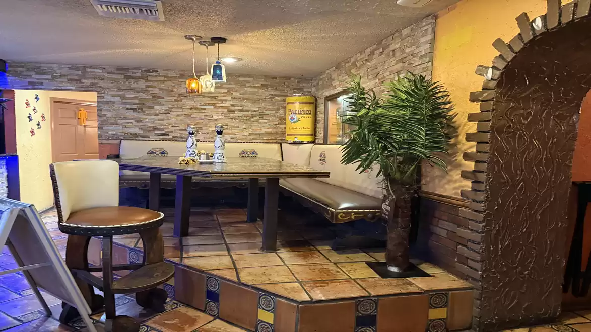 Cozy restaurant with stone and wood interior, decorated with plants and bottles on the table.
