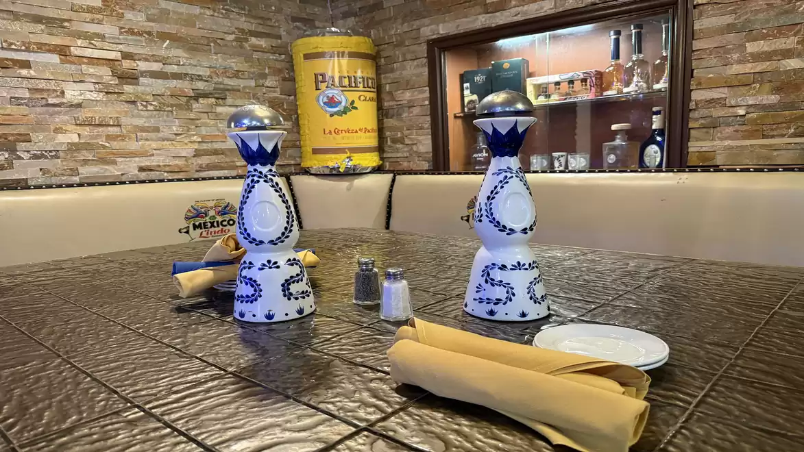 A table in a Mexican restaurant with decorative bottles, yellow napkins, and a rustic ambiance.