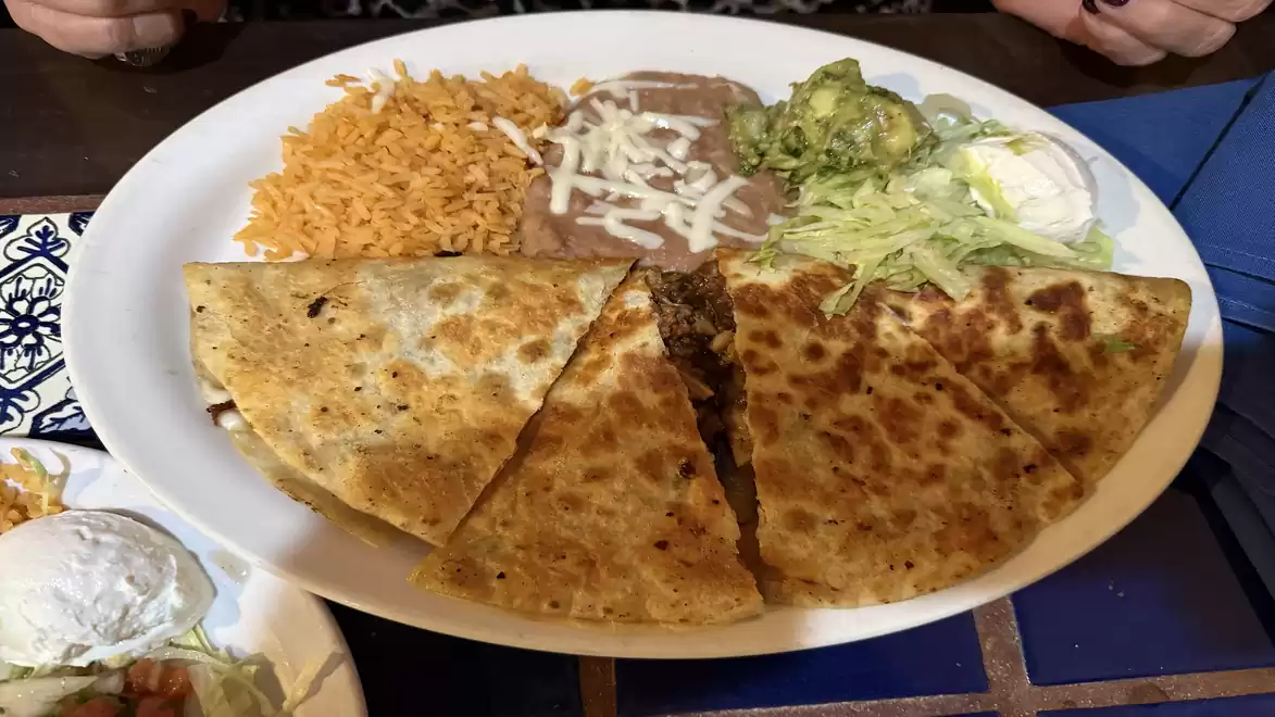 Plate of quesadillas served with rice, beans, guacamole, salad, and sour cream.