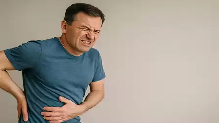 A man in a blue t-shirt is holding his stomach and appears to be in pain.