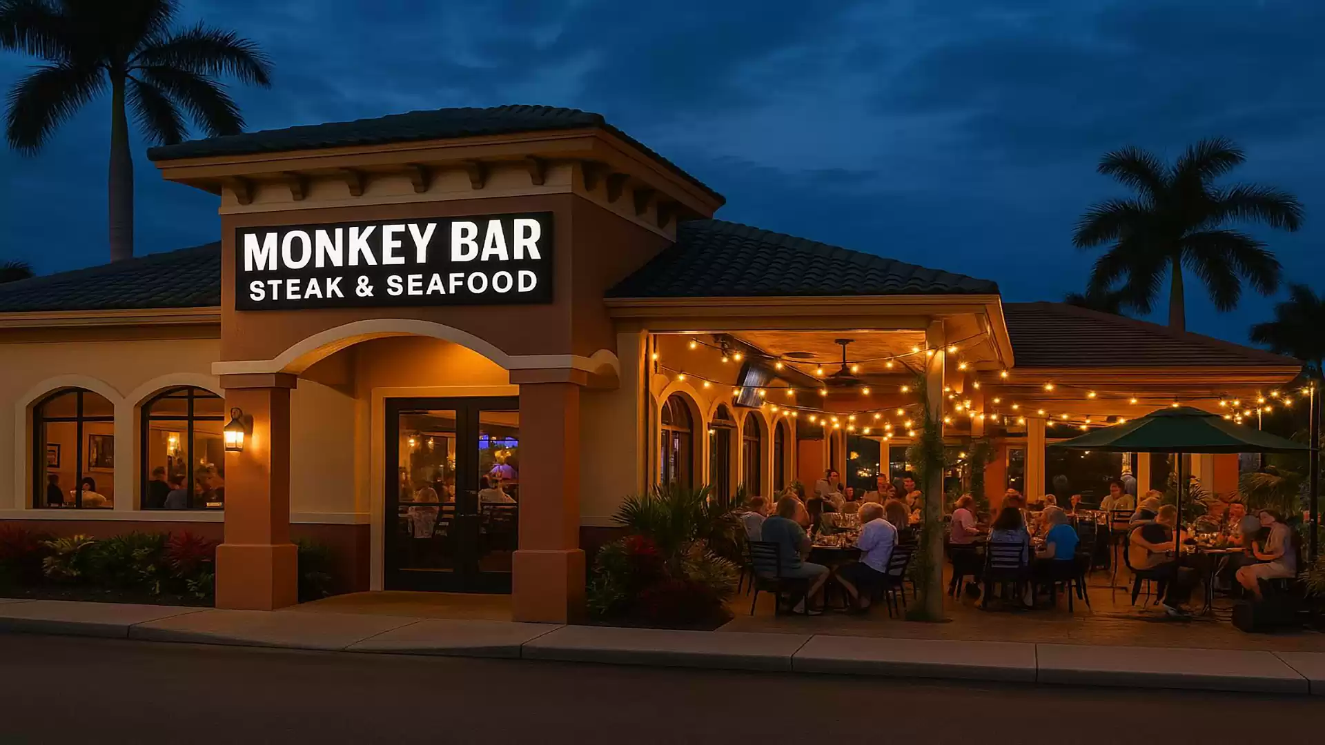 Exterior view of the Monkey Bar Steak & Seafood in the evening with a lit outdoor area and guests dining under string lights.