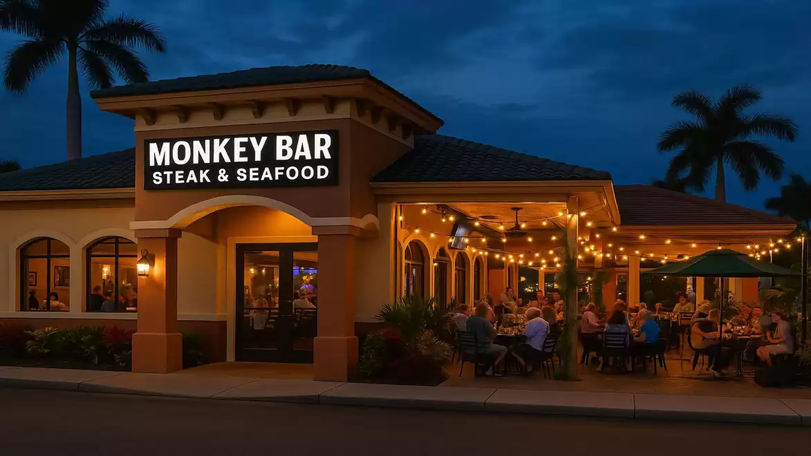 Exterior view of the Monkey Bar Steak & Seafood in the evening with a lit outdoor area and guests dining under string lights.