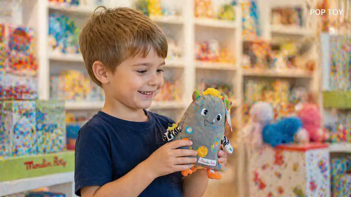 A smiling boy holds a colorful stuffed toy in a toy store.