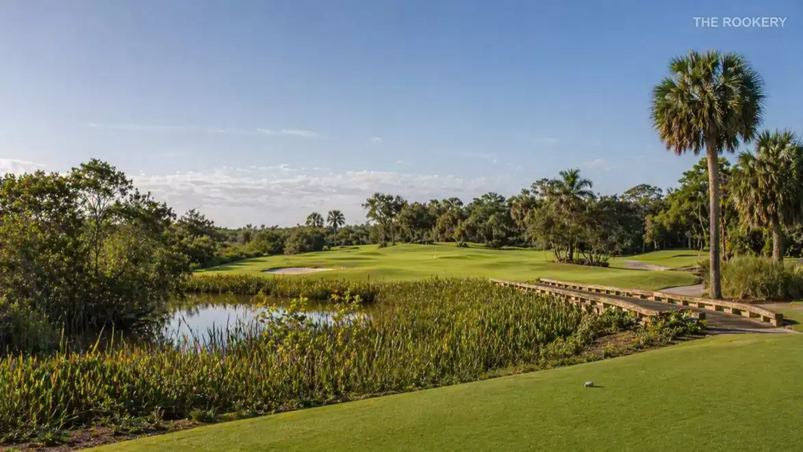 Golf course with palm trees, water hazard, and sunny sky.