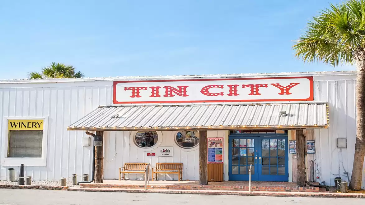 Exterior view of Tin City, a shopping area with blue skies in the background and palm trees on the sides.