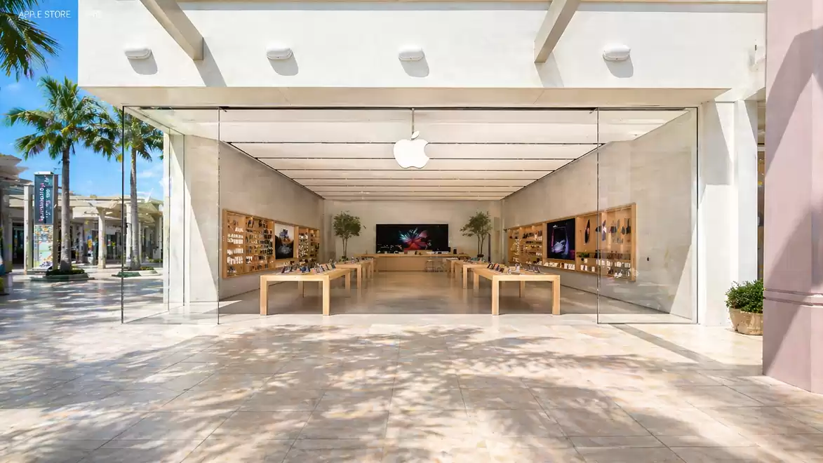 Modern store with open glass entrance, palm trees, and blue sky in the background. Minimalist interior design with wood and high-tech products.