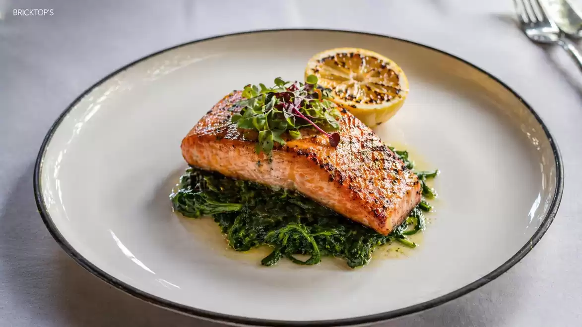 A plate with grilled salmon fillet on a bed of sautéed spinach, served with a grilled half lemon.