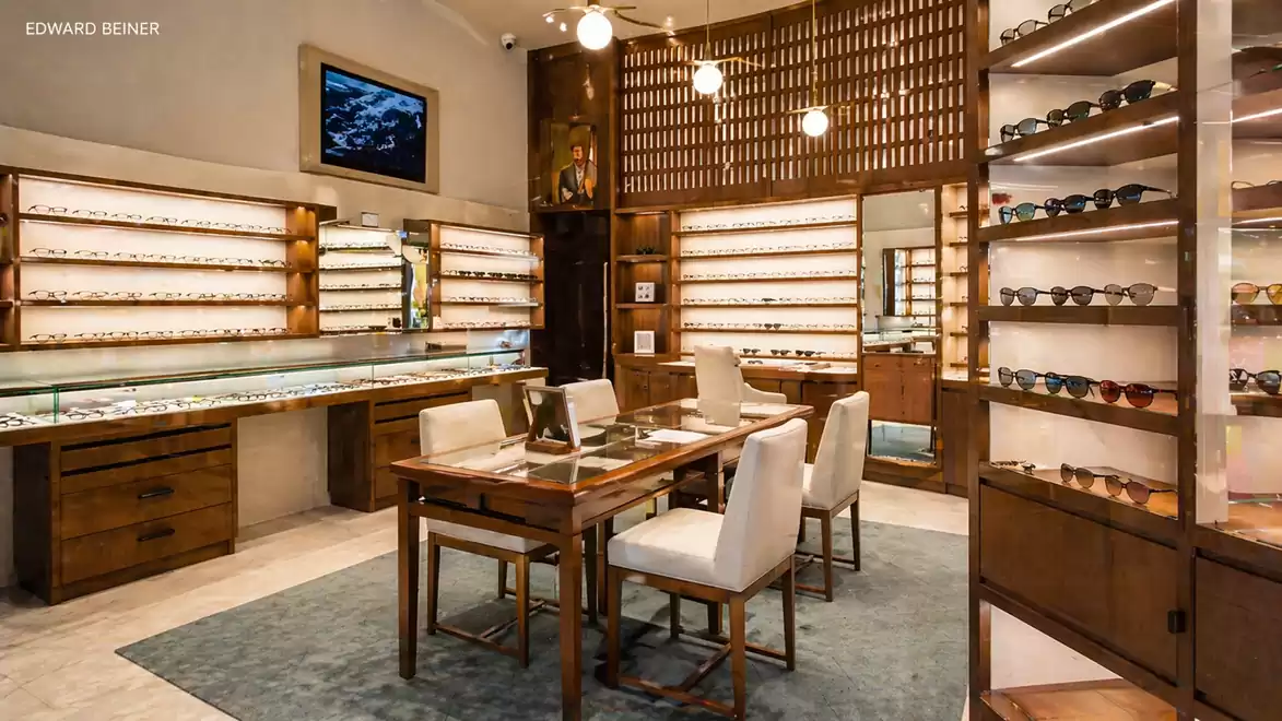 Elegant eyewear store with wooden furniture, glass displays, and white cushioned chairs in a warm, inviting atmosphere.