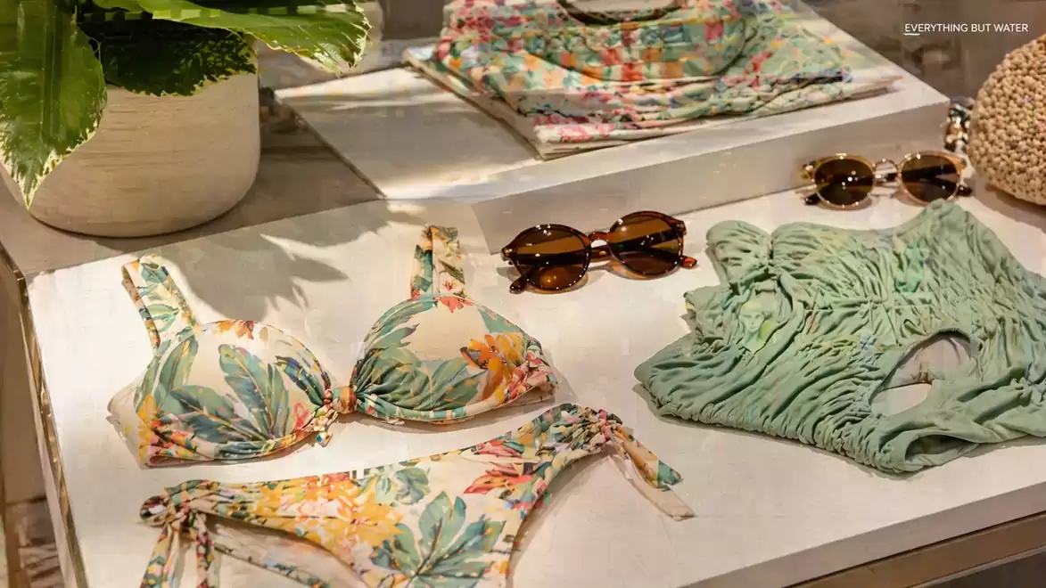 Swimwear and sunglasses on a table decorated with tropical patterns and green leaves, ideal for a beach vacation.
