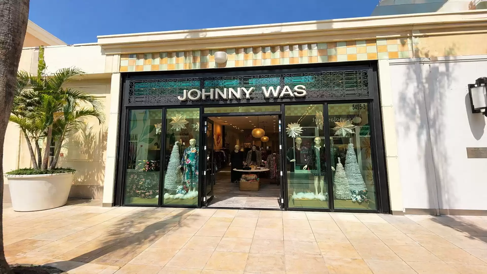 Entrance to a boutique with large glass windows, Christmas decorations, and a sign 'Johnny Was'.