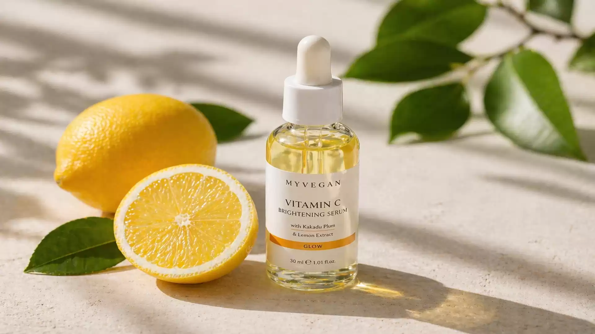A bottle of Vitamin C serum stands on a light surface, surrounded by a lemon cut in half. Green leaves are visible in the background.