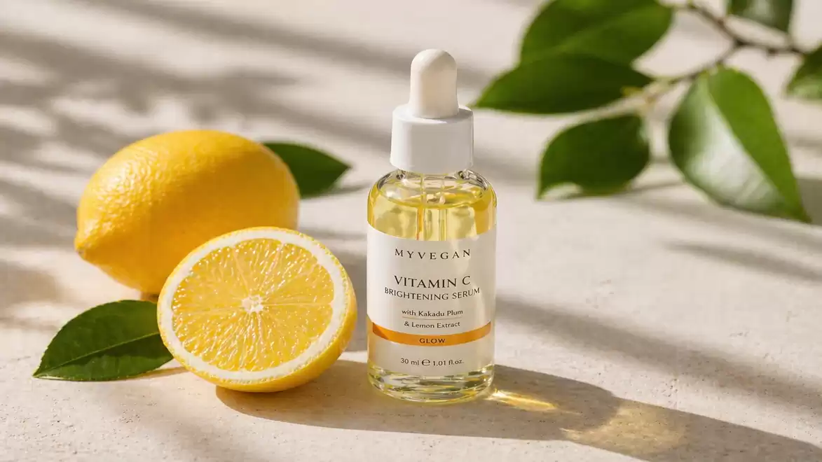 A bottle of Vitamin C serum stands on a light surface, surrounded by a lemon cut in half. Green leaves are visible in the background.