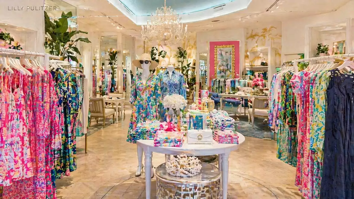 An elegant fashion store with a variety of colorful dresses on clothing racks. A central table displays folded garments and decorative items. Luxurious lighting hangs from the ceiling.