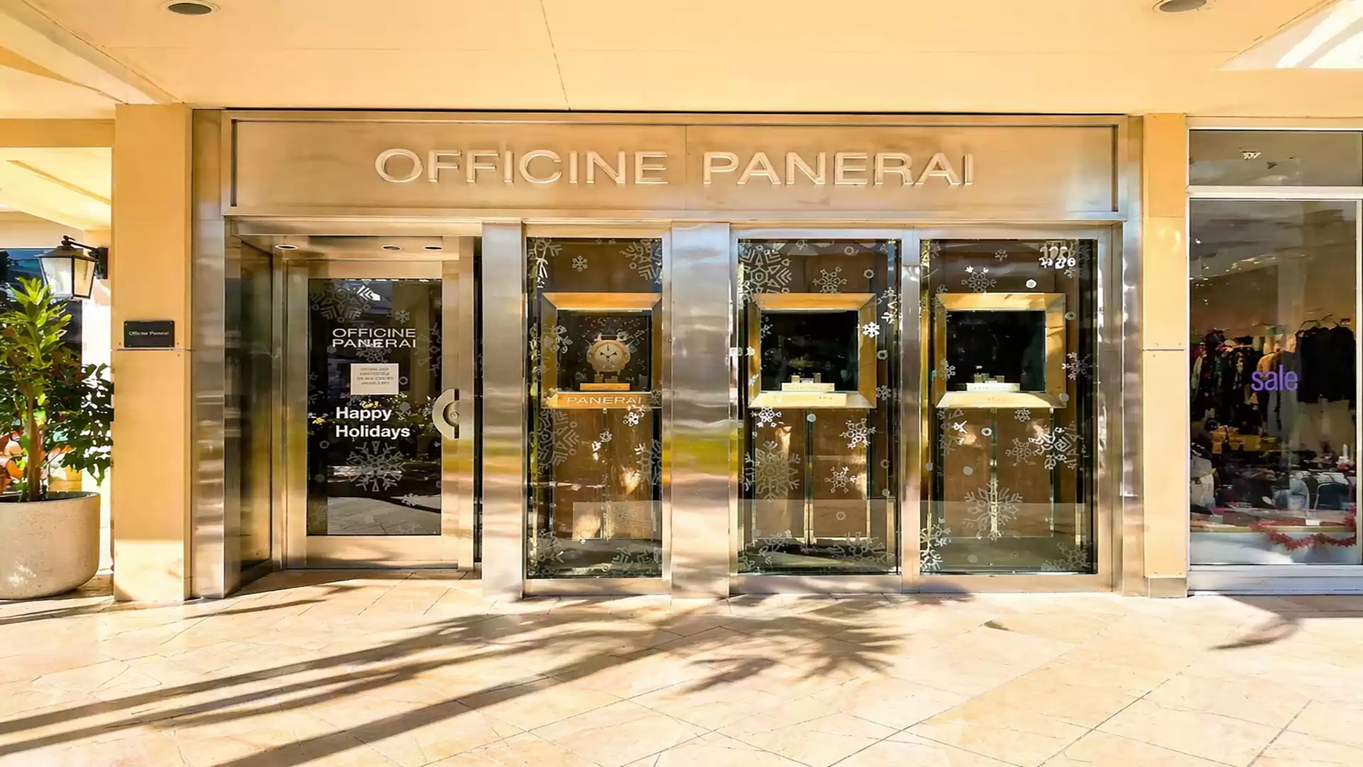 Entrance of a luxury watch store with the brand Officine Panerai, shiny glass facade, and festive holiday decorations.