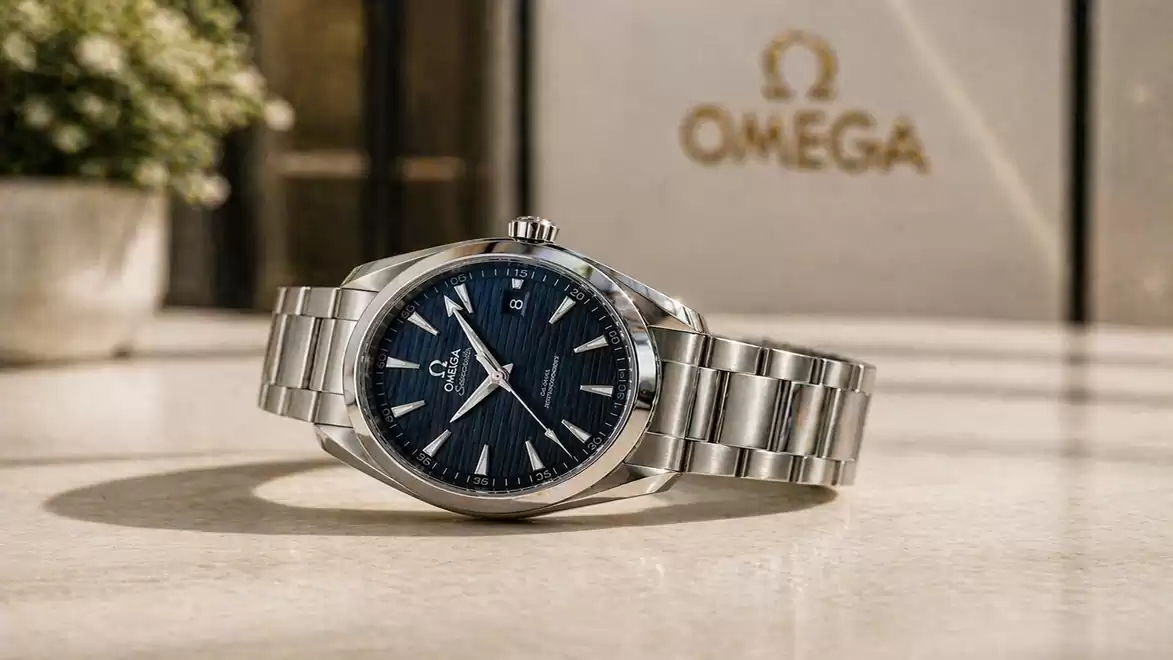 Elegant wristwatch with a blue dial and silver band displayed on a table with a blurred background and Omega logo.