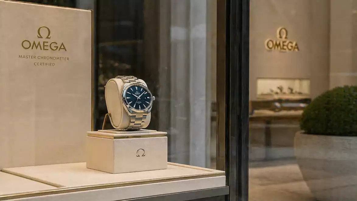 An Omega watch with a blue dial displayed in a showcase in front of a store with the Omega logo.